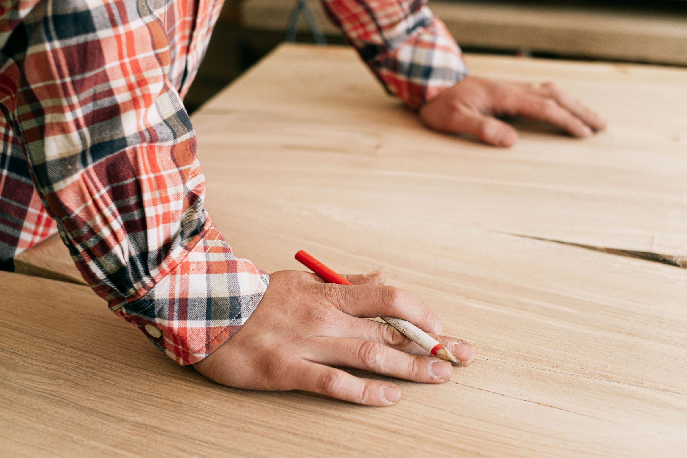 Hand reißt mit rotem Zimmermannsstift eine Linie auf einem Holzbrett an